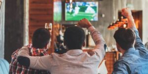 Friends cheering while watching a sports event on TV, highlighting the excitement of sports betting.