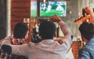 Friends cheering while watching a sports event on TV, highlighting the excitement of sports betting.