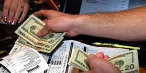 Person handling cash while placing sports bets, with betting slips and odds sheets on the table