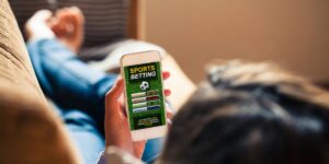 Person relaxing on a couch while using a smartphone to browse a sports betting app with match betting options.