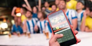 Fan using a mobile betting app in a sports bar surrounded by cheering football supporters.