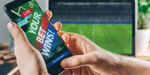 Person holding smartphone displaying a winning sports bet while watching live football match on laptop.