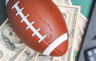AFL betting concept showing an American football placed on US dollar bills beside a notebook, pen, and calculator