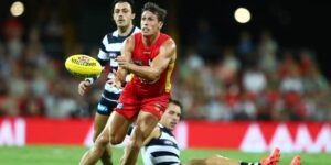 AFL player in red uniform handballing during a professional match against opponents in striped jerseys