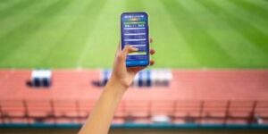 Hand holding a smartphone displaying sports betting odds from an Australian bookmaker at a stadium