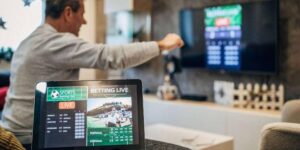 Man celebrating live sports betting results displayed on a tablet while watching a match on TV