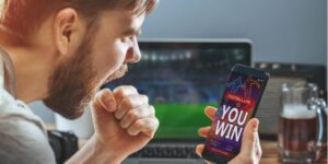Man celebrating after winning a football bet on his smartphone.