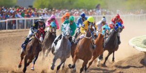 Group of racehorses and jockeys in colourful silks sprinting on a dirt track during a competitive horse race 