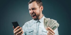 Excited man celebrates while holding cash and checking his smartphone, representing a winning betting moment influenced by personalized AI insights. 