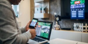 Man using laptop and smartphone for live sports betting while watching a match on television.
