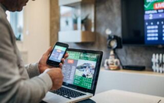 Man using laptop and smartphone for live sports betting while watching a match on television.