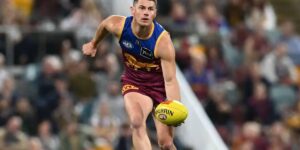 An AFL player from the Brisbane Lions runs with the ball during a match, focused on advancing play.