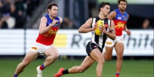 A Collingwood Magpies player runs with the ball while being chased by Brisbane Lions opponents during an AFL match.