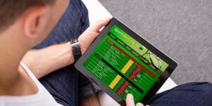 A man using a tablet displaying a sports betting interface with odds and match listings across various sports.