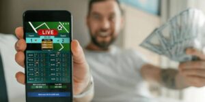 Person showing a mobile phone with a live betting screen while holding cash in the other hand.