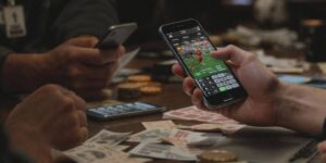 People using mobile phones to place sports bets at a table with betting slips and money.