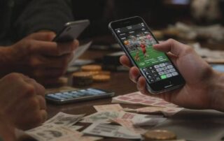 People using mobile phones to place sports bets at a table with betting slips and money.