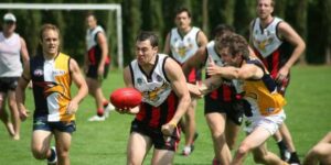 Players competing in an Australian rules football match with one player running forward holding the ball.