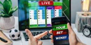 Person holding a phone showing a winning fixed odds bet while a live betting screen is open on a laptop in the background.