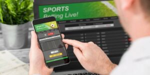 Person using a smartphone betting exchange app in front of a laptop showing live sports betting markets